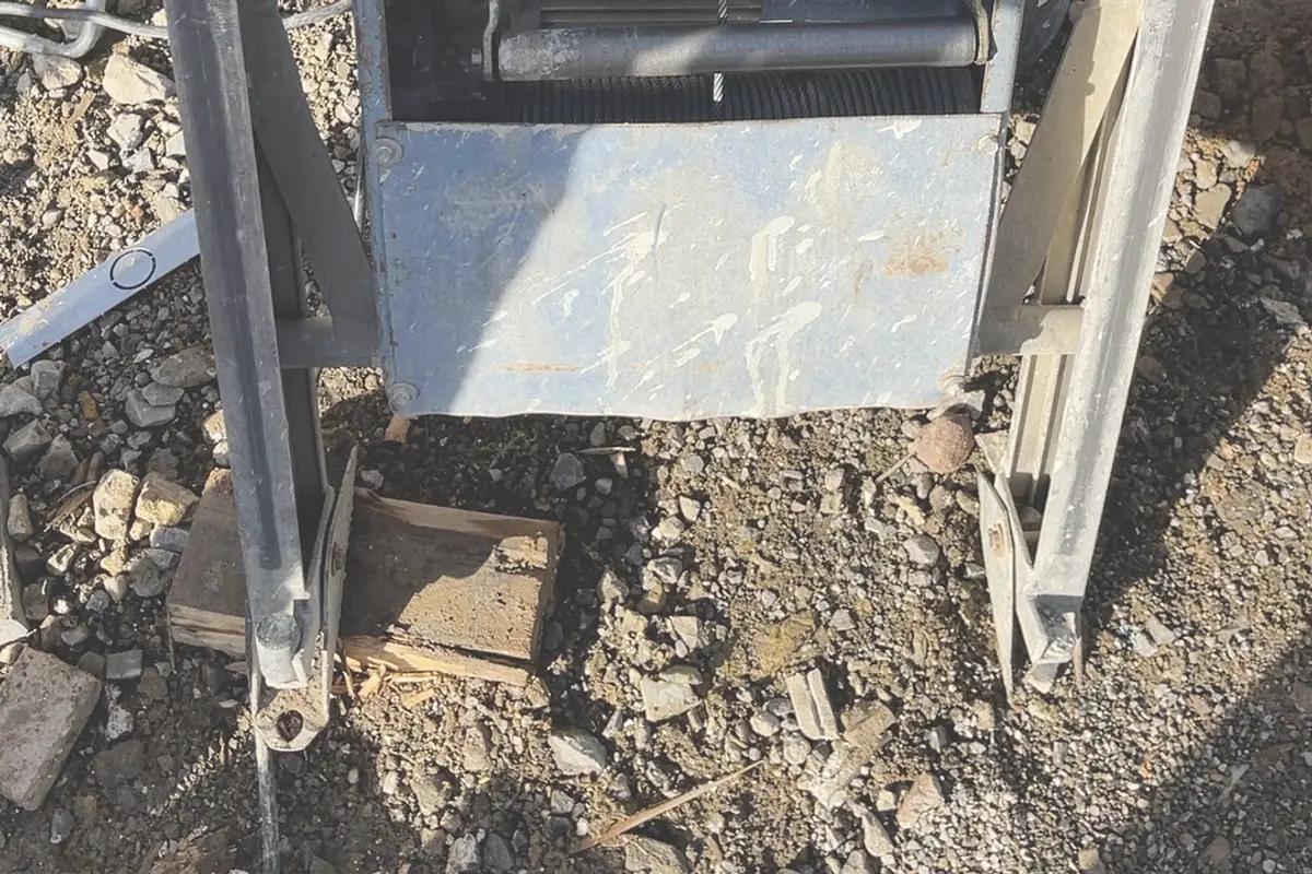 Montacarichi inclinato in cantiere, un piede d'appoggio poggia su pezzi di legno sciolti nella ghiaia